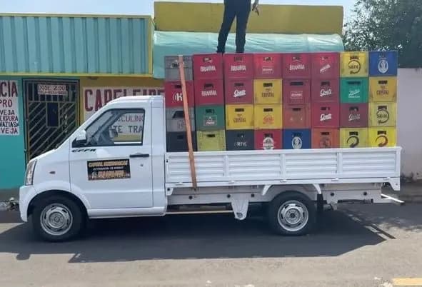Picape V21 com a caçamba carregada de engradados de bebida na porta de um comércio